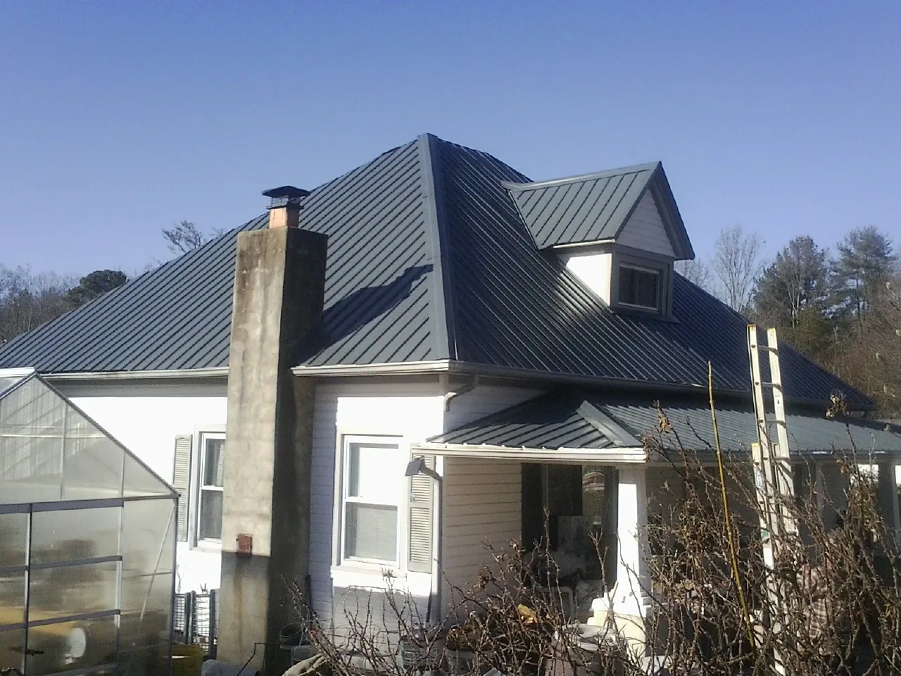 Dark blue standing seam metal roof on a white farmhouse with dormer — Slate & Tile Roof Repair by Roofing Brothers in Saint Peter