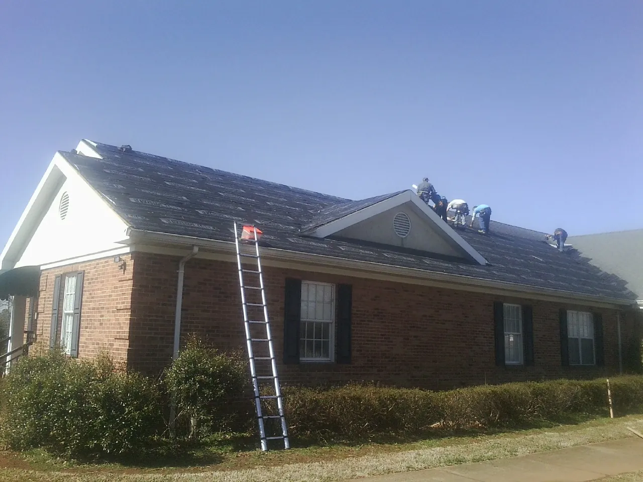 Crew tearing shingles off a brick ranch roof with a ladder set — Metal Roof Repair work by our crew in Saint Peter