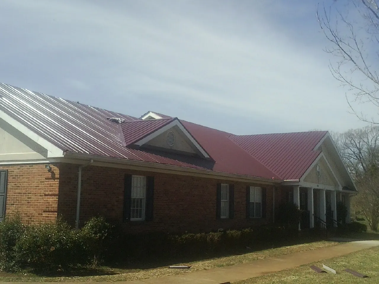 Red metal roof with gabled entries on a long brick building, from a Hail Damage Roof Repair job in Saint Peter