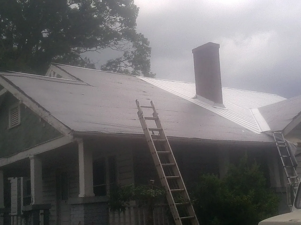 Ladders against a metal roof on an older home with a brick chimney in Saint Peter