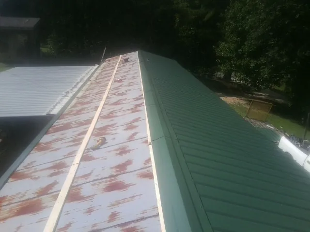 Old rusted panels beside newly installed green metal roofing — Wind Damage Roof Repair by Roofing Brothers in Saint Peter