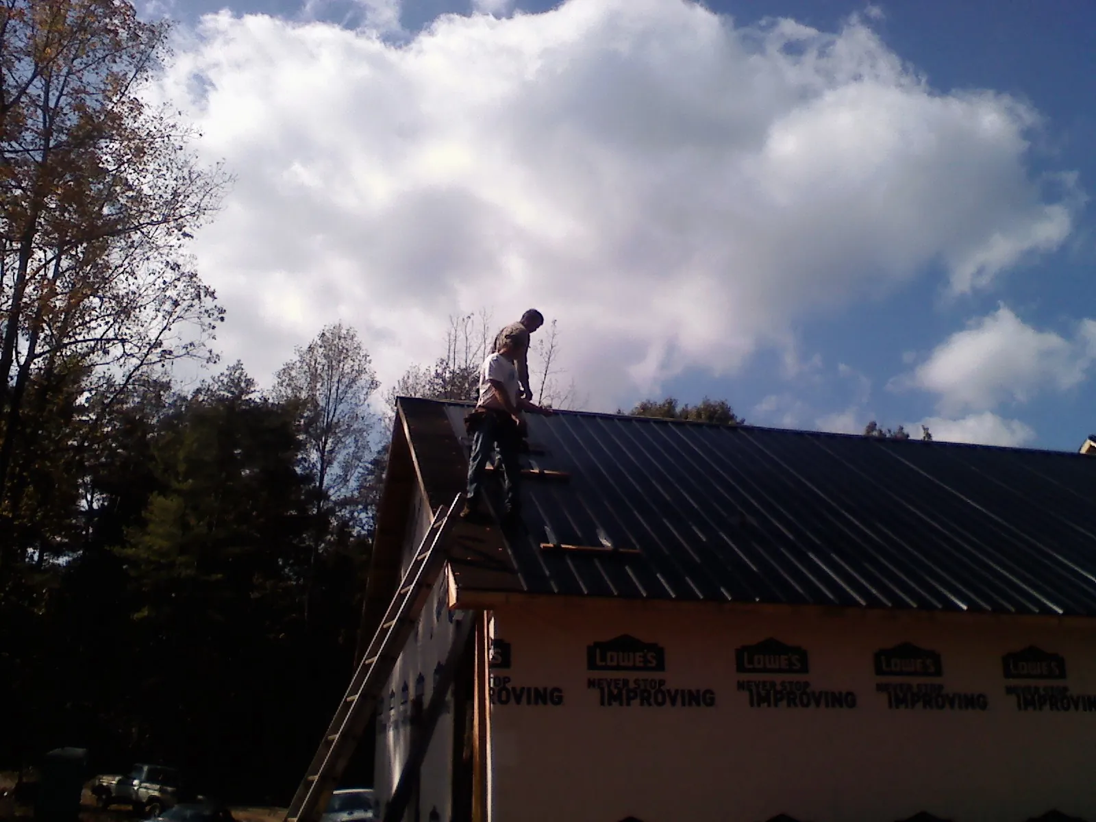 Roofer fastening dark metal panels high against a cloudy sky, from a Roof Inspection job in Saint Peter
