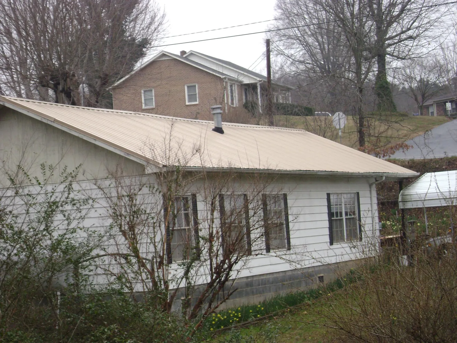 Tan metal roof on a white sided house set into a hillside — Commercial Roofing by Roofing Brothers in Saint Peter