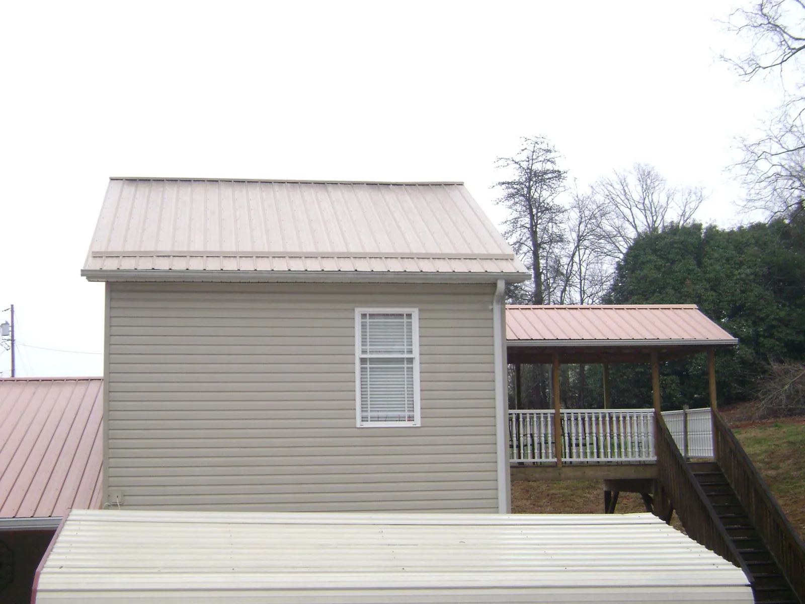 Tan metal roofs on a two story addition and attached porch, from a Roof Replacement job in Saint Peter